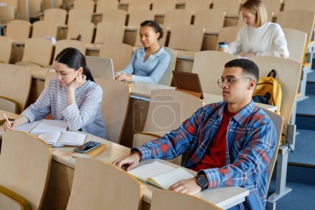 Photo for Group of students sitting at desk with books in lecture hall and studying at university - Royalty Free Image