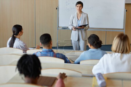 Mature teacher explaining new topic to students during lecture in lecture hall of college