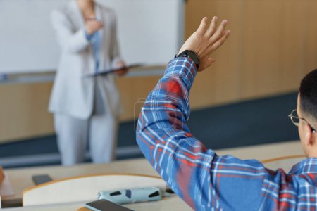 Photo for Rear view of student raising his arm and answering at lecture while teacher asking to him - Royalty Free Image
