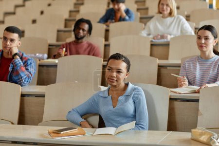 Photo for Group of students sitting at desk with books and listening to teacher at lecture at college - Royalty Free Image
