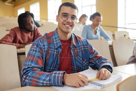 Photo for Portrait of schoolboy in eyeglasses smiling at camera while sitting at desk at lecture - Royalty Free Image