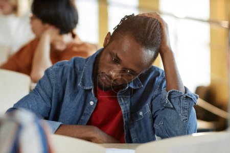 Téléchargez les photos : Afro-Américain stressé étudiant assis au bureau en classe et examen d'écriture à l'université - en image libre de droit