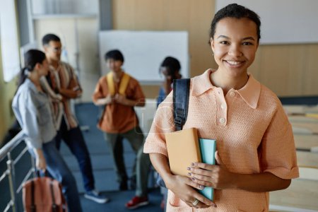 Photo for Portrait of smiling student looking at camera while standing in lecture hall with her classmates in background - Royalty Free Image