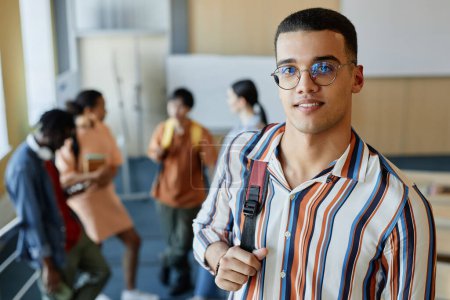 Photo for Portrait of student in eyeglasses with backpack smiling at camera standing in lecture hall at college - Royalty Free Image