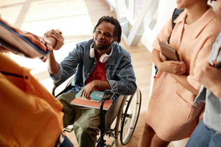 Téléchargez les photos : Étudiant afro-américain handicapé assis en fauteuil roulant et saluant ses camarades de classe pendant la pause au collège - en image libre de droit