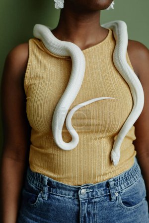 Cropped shot of young African American woman with white rat snake creeping over her on neck and chest standing in front of camera