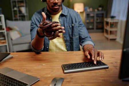 Téléchargez les photos : Gros plan d'un jeune homme d'affaires avec un serpent de rat enlacant sa main en appuyant sur la touche du clavier de l'ordinateur alors qu'il était assis à côté du bureau devant le moniteur - en image libre de droit