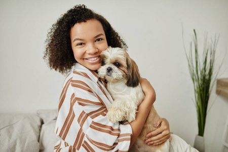 Foto de Candid cintura hacia arriba retrato de negro joven mujer sosteniendo lindo perro y sonriendo a la cámara en casa - Imagen libre de derechos