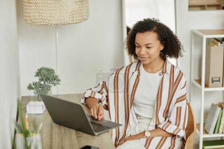 Téléchargez les photos : Portrait de jeune femme noire utilisant un ordinateur portable au bureau à la maison dans un intérieur blanc minimal, espace de copie - en image libre de droit