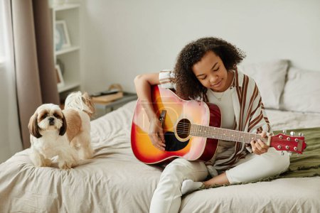 Photo for Minimal portrait of black young woman playing acoustic guitar and relaxing at home with little pet dog, copy space - Royalty Free Image