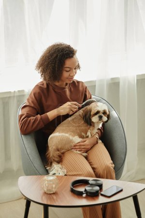 Foto de Retrato vertical de una joven negra cepillando a un lindo perrito en casa y disfrutando del cuidado de mascotas - Imagen libre de derechos