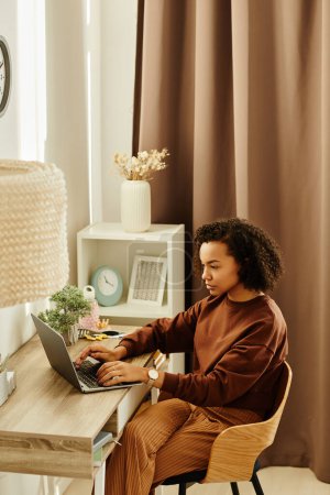 Photo for Vertical portrait of black young woman using laptop in cozy home interior - Royalty Free Image
