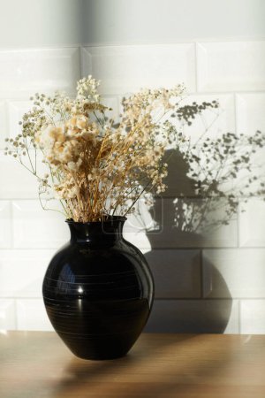 Foto de Imagen vertical de ramo de flores secas en jarrón negro de pie sobre la mesa en la habitación - Imagen libre de derechos