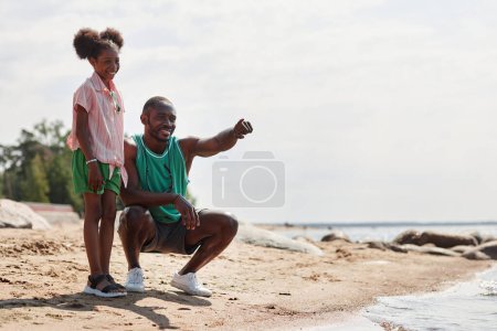 Téléchargez les photos : Papa afro-américain marchant avec sa fille sur la plage, ils profitent de leurs vacances d'été - en image libre de droit