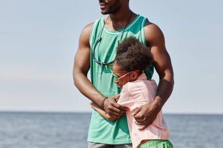 Téléchargez les photos : Petite fille embrassant son père pendant qu'ils marchent ensemble le long de la plage à l'extérieur - en image libre de droit