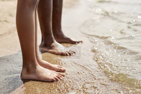 Foto de Primer plano de papá descalzo de pie sobre la arena cerca del agua junto con su hijo - Imagen libre de derechos