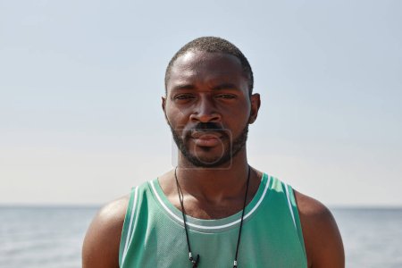 Téléchargez les photos : Portrait d'un bel homme afro-américain regardant la caméra alors qu'il se tenait sur la plage par une journée ensoleillée - en image libre de droit