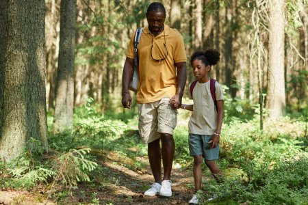 Photo for African American dad walking along the footpath with his daughter in the forest during their travelling on the nature - Royalty Free Image