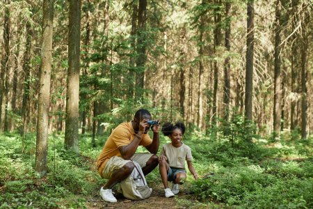 Photo for Dad looking through binoculars while hiking with his daughter in the forest - Royalty Free Image