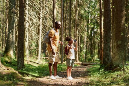 Téléchargez les photos : Petite fille regardant à travers les jumelles pendant le voyage avec son père dans la forêt - en image libre de droit