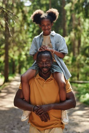 Foto de Imagen vertical de papá sonriendo a la cámara mientras camina junto con su hija en el bosque - Imagen libre de derechos