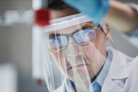 Téléchargez les photos : Gros plan du scientifique masculin portant un écran facial en laboratoire lors d'expériences avec une éprouvette - en image libre de droit