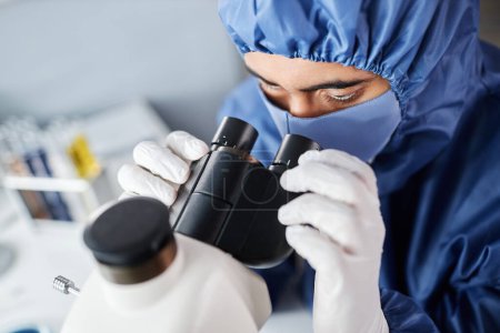 Foto de Primer plano del científico que mira en el microscopio mientras usa equipo de protección en el laboratorio, espacio de copia - Imagen libre de derechos