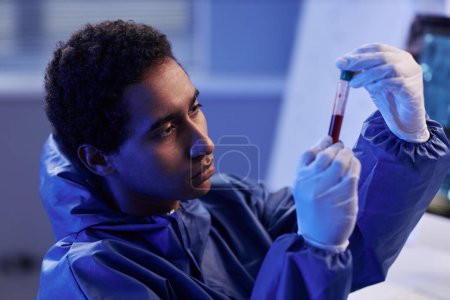 Photo for Side view portrait of young male scientist holding test tube with red liquid in neon light while doing research in laboratory - Royalty Free Image