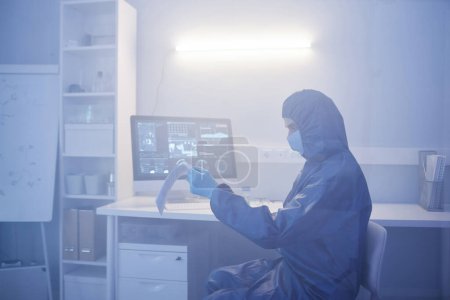 Photo for Side view portrait of scientist wearing full protective suit working at desk in biohazard dange zone, copy space - Royalty Free Image