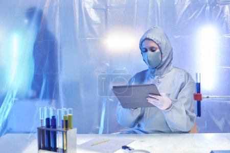 Photo for Female scientist wearing full protective suit working at desk in biohazard dange zone, copy space - Royalty Free Image