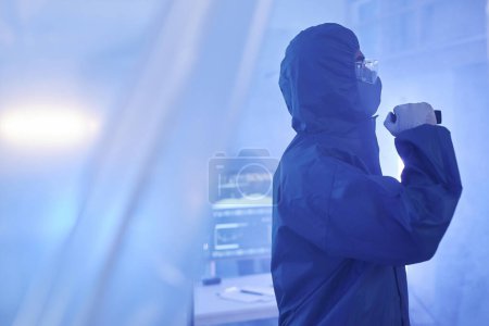 Photo for Blue tone portrait of worker wearing full protective suit entering biohazard danger zone with flashlight, copy space - Royalty Free Image