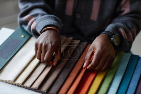 Téléchargez les photos : Gros plan du designer afro-américain choisissant la couleur dans la palette de couleurs tout en étant assis à table - en image libre de droit