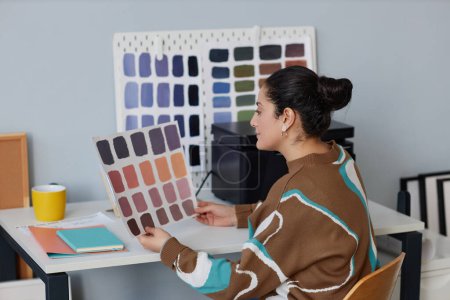 Téléchargez les photos : Designer examinant le modèle de couleur tout en étant assis à son lieu de travail dans le bureau - en image libre de droit