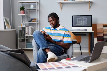 Téléchargez les photos : Concepteur afro-américain travaillant en ligne sur tablette PC tout en étant assis sur un fauteuil dans le bureau - en image libre de droit