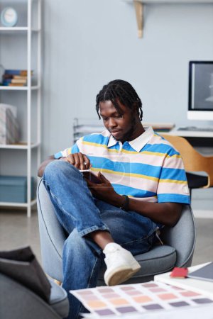 Téléchargez les photos : Image verticale du graphiste afro-américain travaillant sur tablette PC assis sur un fauteuil au bureau - en image libre de droit