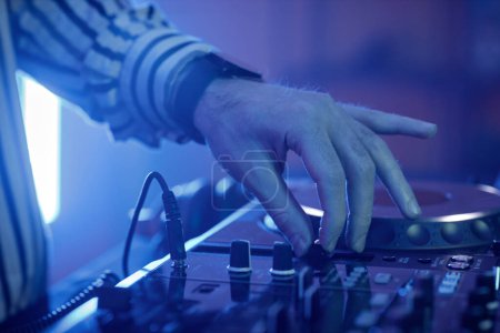 Foto de Vista lateral de primer plano de DJ masculino ajustando interruptores en el tocadiscos en luces de neón en la fiesta disco, espacio de copia - Imagen libre de derechos