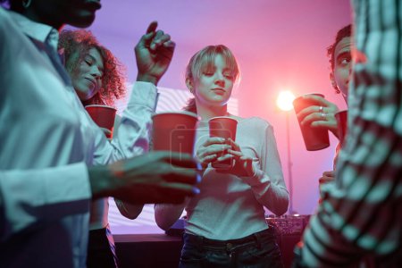 Photo for Diverse group of young people at house party holding red cups with alcohol and dancing in neon light - Royalty Free Image
