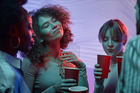 Foto de Retrato en la cintura de chicas guapas bailando en la fiesta de la casa y sosteniendo copas rojas con alcohol - Imagen libre de derechos