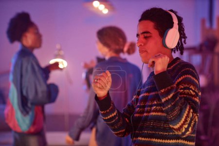 Foto de Retrato de cintura hacia arriba de un joven étnico bailando con auriculares mientras disfruta de una fiesta disco silenciosa con luz de neón, espacio para copiar - Imagen libre de derechos