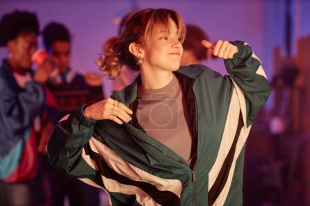 Foto de Retrato de la cintura hacia arriba de una chica joven vestida con un atuendo retro bailando en la fiesta disco de los 80 con luces rosas - Imagen libre de derechos