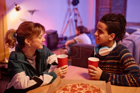 Téléchargez les photos : Portrait latéral de jeune couple mangeant de la pizza et bavardant à la fête maison rétro - en image libre de droit