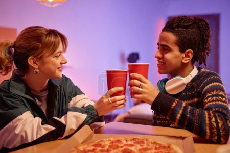 Foto de Retrato de vista lateral de pareja joven retro comiendo pizza y tostadas con tazas de papel rojo - Imagen libre de derechos