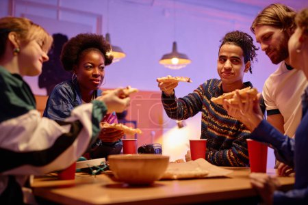 Téléchargez les photos : Groupe diversifié de jeunes mangeant de la pizza à la maison fête style années 80, espace de copie - en image libre de droit