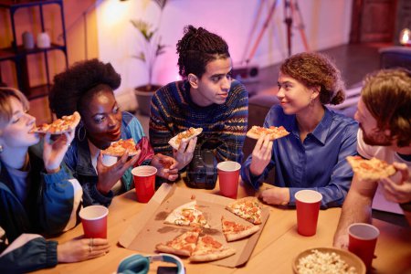 Foto de Vista de ángulo alto en el grupo de jóvenes comiendo pizza en la fiesta de la casa estilo 80 - Imagen libre de derechos
