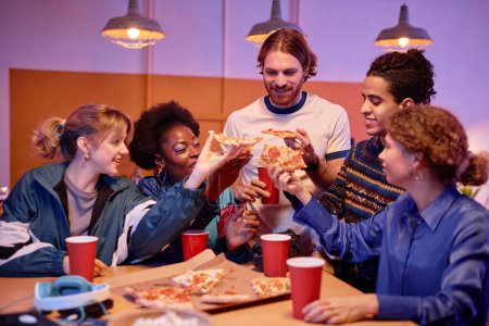 Foto de Diverso grupo de jóvenes comiendo pizza en la fiesta de la casa al estilo de los 80 - Imagen libre de derechos