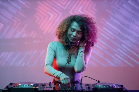 Photo for Portrait of curly haired young woman as female DJ making music tracks at disco party in neon light, copy space - Royalty Free Image