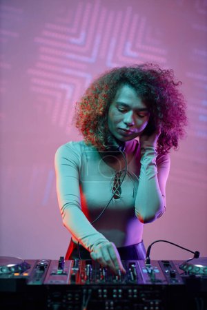 Photo for Portrait of young woman DJ making music tracks at nightclub in neon light - Royalty Free Image