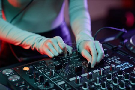 Téléchargez les photos : Gros plan jeune femme comme DJ faisant des pistes musicales à la table de mixage à la lumière du néon - en image libre de droit