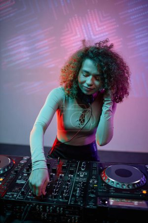 Photo for Vertical portrait of young woman as DJ making music tracks at disco party in neon light - Royalty Free Image