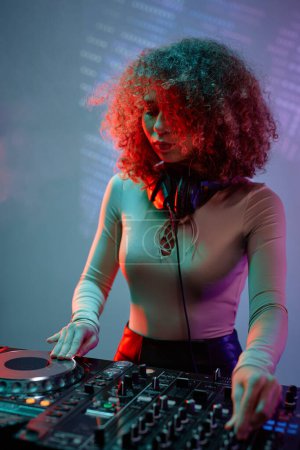 Photo for Vertical portrait of curly haired young woman as female DJ making music in neon light - Royalty Free Image
